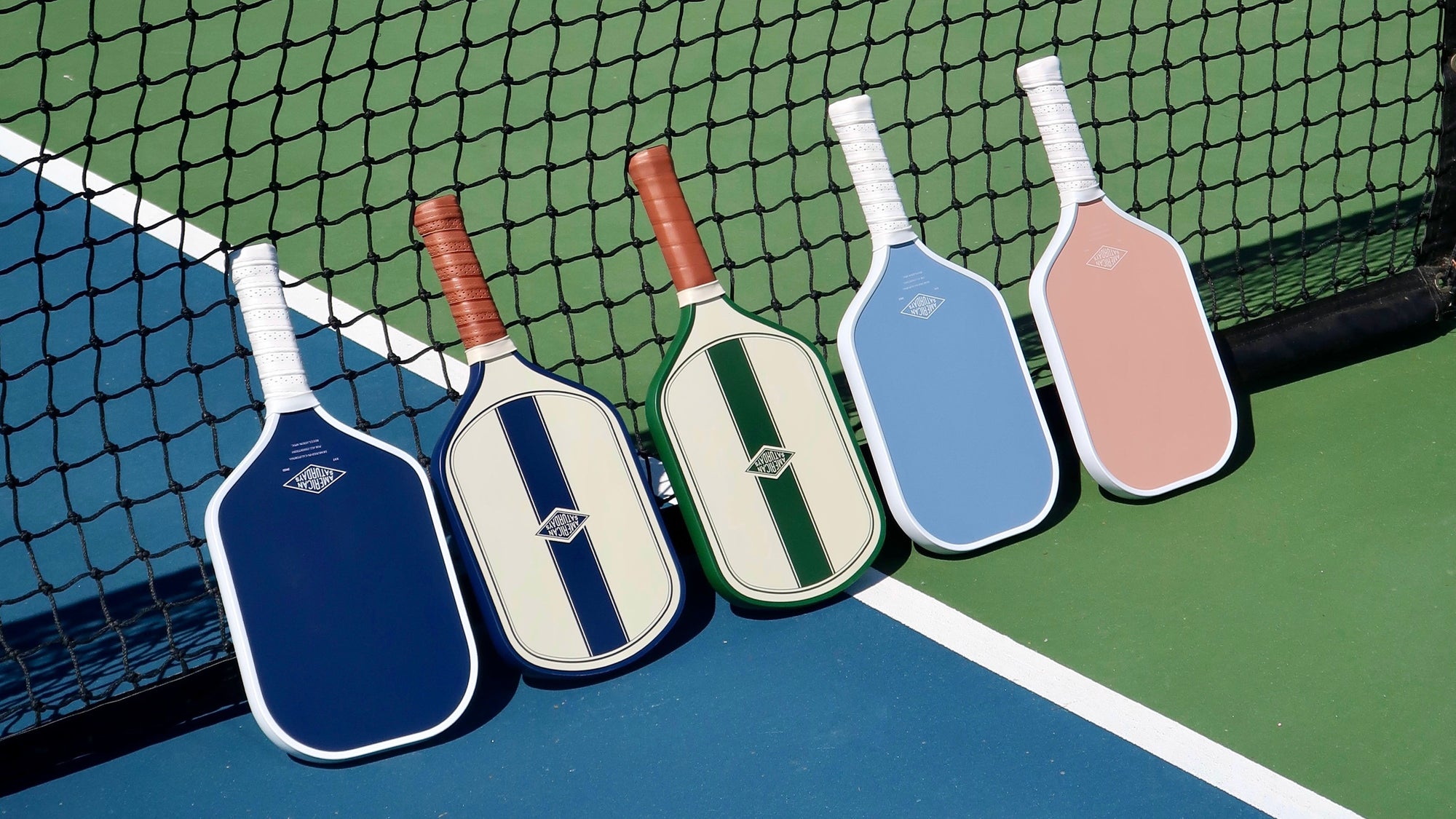 American Saturdays Pickleball paddles leaning against the net of a pickleball court