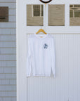 A white long-sleeve crewneck sweatshirt with a small navy graphic on the left chest, hanging on a wooden hanger in front of a white barn-style door.